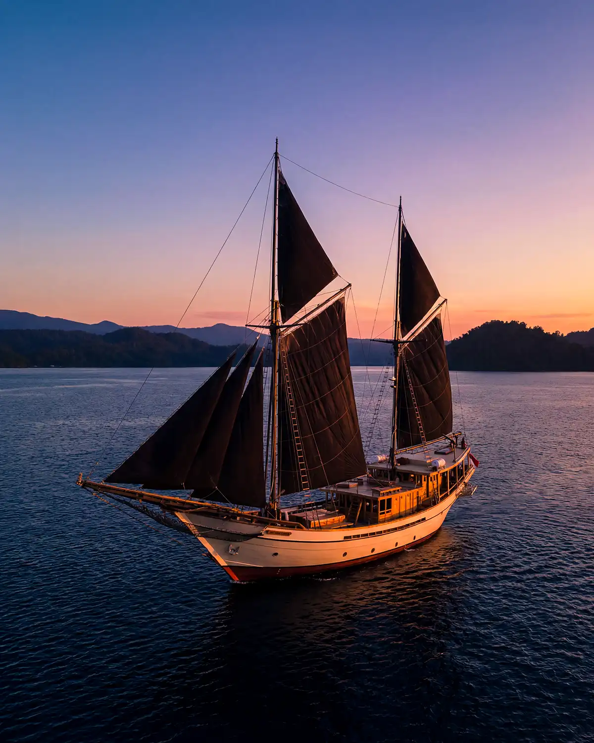 A black-sailed phinisi at dusk in Komodo